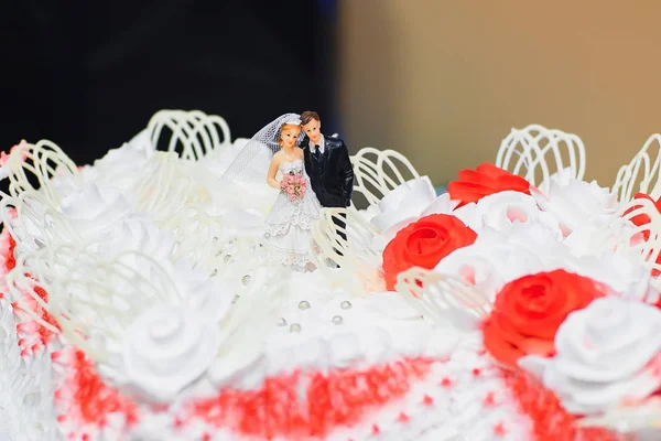 Bolo de casamento creme branco decorado com rosas vermelhas com figuras da noiva e do noivo — Fotografia de Stock
