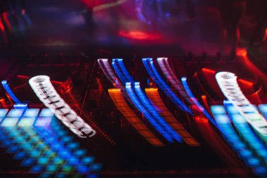 Bir gece kulübünde DJ mikserinde kumanda ve düğmelerden parlayan renkli ışıklar