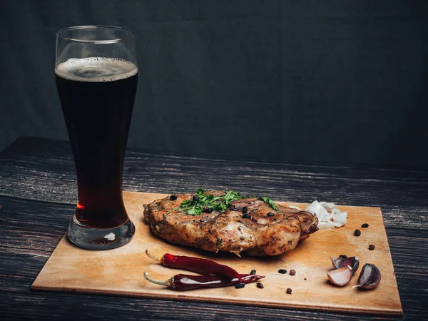 Gekookt varkensvlees met een glas donker bier en andere ingrediënten op een houten plank — Stockfoto