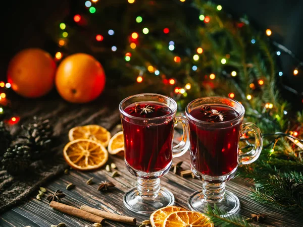 Mulled κρασί σε ποτήρια με φέτες πορτοκαλιού και τα μπαχαρικά σε ένα ξύλινο τραπέζι με μια Χριστουγεννιάτικη γιρλάντα. Παραδοσιακό αλκοολούχο ποτό — Φωτογραφία Αρχείου