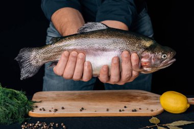 Erkek mutfak arka plan üzerinde elinde balık. Büyük taze alabalık