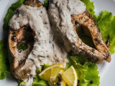 Beyaz plaka üzerinde krema soslu kızarmış alabalık. Limon ve salata kırmızı balık