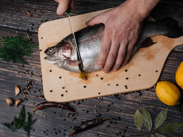 El hombre corta una trucha con un cuchillo en una tabla. Pescado crudo fresco — Foto de Stock