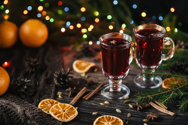 Copos com vinho quente em uma mesa de madeira decorada com árvores de Natal. Bebida alcoólica tradicional de inverno com fatias de laranja — Fotografia de Stock