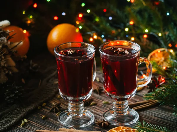 Dos copas con vino caliente en una mesa de madera con naranja, canela, cardamomo, estrellas de anís. Bebida alcohólica caliente de invierno tradicional — Foto de Stock