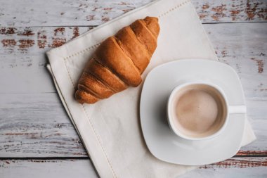 Beyaz fincan kahve ve kruvasan ahşap masa üzerinde. Sabahları geleneksel Fransız kahvaltı