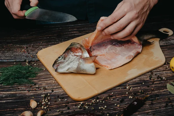 man cuts knife red fish on wooden Board