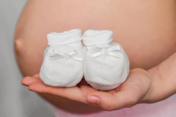 Mãos de uma mulher grávida com botas para um recém-nascido — Fotografia de Stock