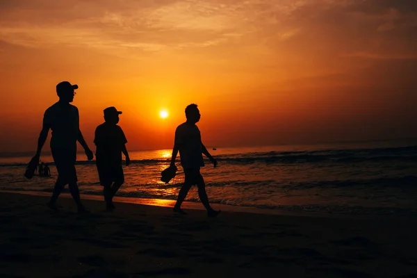 Gündoğumu arka plan üzerinde denizin kenarında sahildeki adamlar siluetleri — Stok fotoğraf