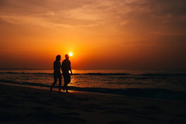 Silhouettes of a couple in love on the beach by the sea — Stock Photo, Image