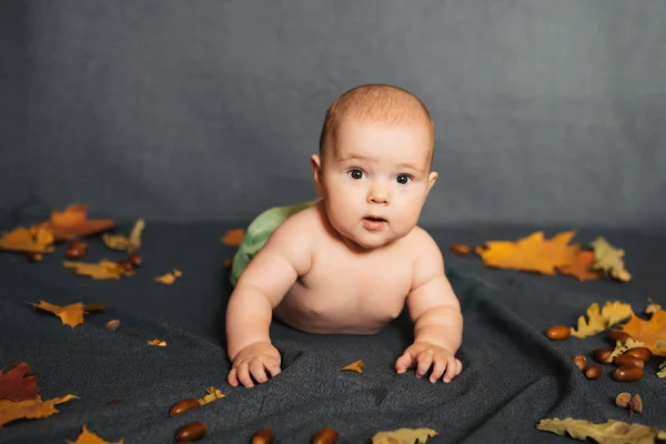 Menino recém-nascido encontra-se no fundo do outono com folhas de bordo e bolota — Fotografia de Stock