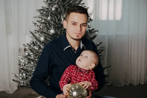 Bambino bambino tra le braccia del padre sullo sfondo dell'albero di Natale — Foto Stock