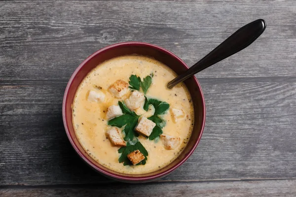 Vegetable pumpkin cream soup with crackers in a bowl with a spoon on a wooden table — Stock Photo, Image