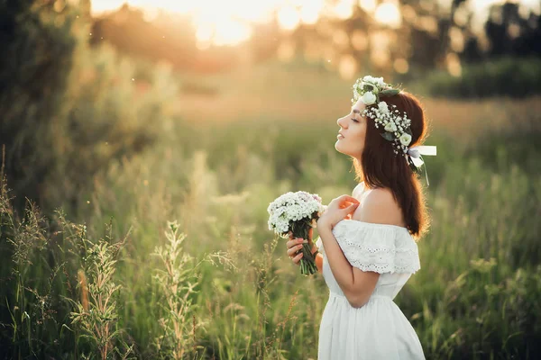 Caucásico chica feliz en un vestido blanco con un ramo de flores y una corona en el verano —  Fotos de Stock