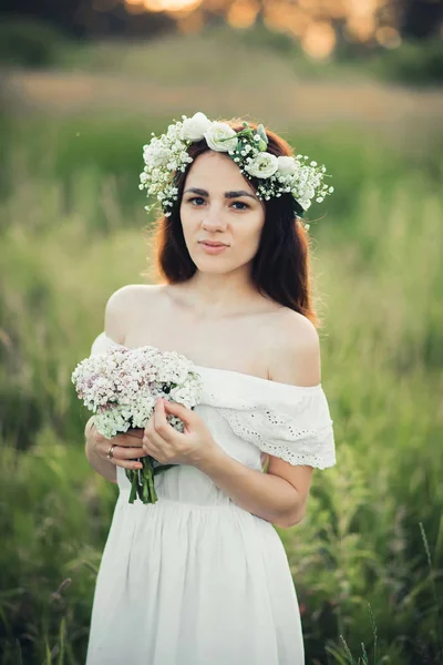 Piękna młoda dziewczyna z bukietem kwiatów i wieniec w białej sukni — Zdjęcie stockowe