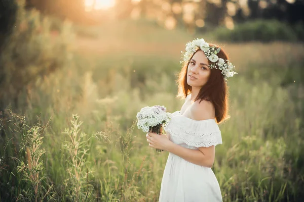 Portrait d'une jolie fille en robe blanche avec un bouquet de fleurs et une couronne en été — Photo