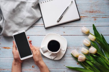 Beyaz Lale buketi bir fincan kahve ve bir smartphone kadın el ve ahşap bir masa üstünde boş bir defter ile