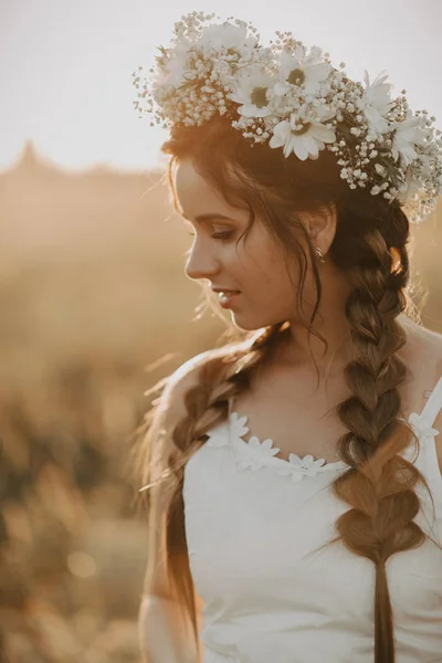 花の花輪および日没時夏の畑の白いドレスの組みひもと魅力的な女の子の肖像画 — ストック写真