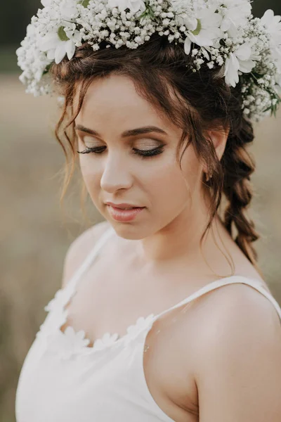 Retrato de uma menina com tranças e uma coroa floral em um vestido de boho branco no verão ao ar livre — Fotografia de Stock