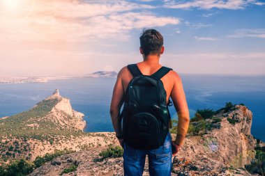 gökyüzüne ve denize karşı dağların üstünde bir sırt çantası olan bir adamın geri
