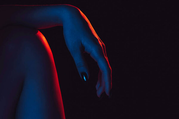 Female hand on knee close up with red blue neon light on black background