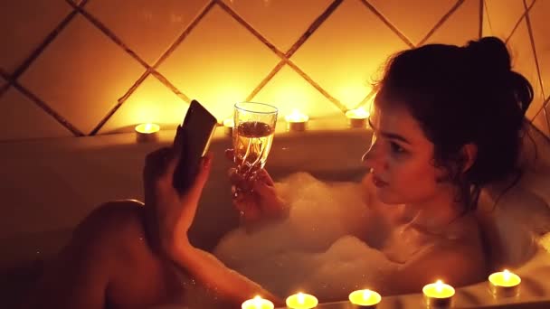 krásná dívka pozitivní bruneta si na smartphone ve vaně vezme sklenici šampaňského