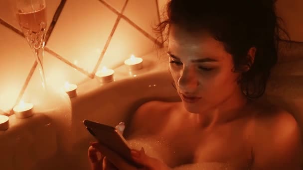 Ung flicka skriver ett meddelande som rör skärmen på smartphone ligger i ett skumbad — Stockvideo