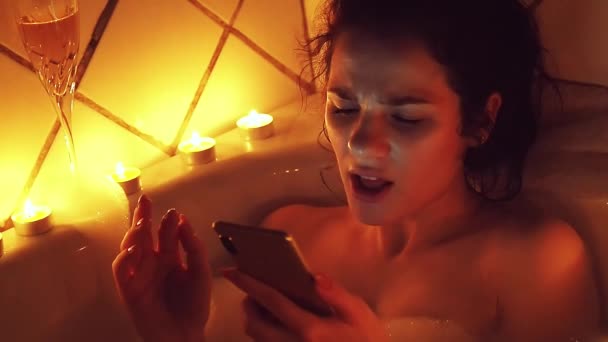Молода дівчина співає слухаючи музику і дивлячись на екран смартфона в піни лазні — стокове відео