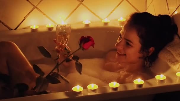 Elinde bir gül ile köpük ile banyoda yatan mutlu güzel genç kız ve şampanya içme — Stok video