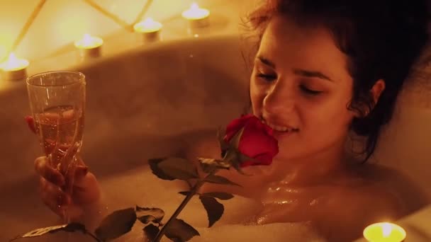 Young girl relaxes having therapy in the bathroom with foam with rose in hand and a glass of wine — 비디오