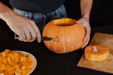 Jack'in Cadılar Bayramı balkabağı. Turuncu balkabağı kesen bıçaklı bir adamın elleri