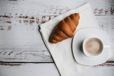 kruvasan ve kahve peçeteye ahşap bir masa üzerinde beyaz bir fincan