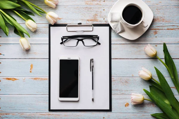 Ramo de tulipanes blancos con un teléfono inteligente, una taza de café y una tableta de papel en una mesa de madera —  Fotos de Stock