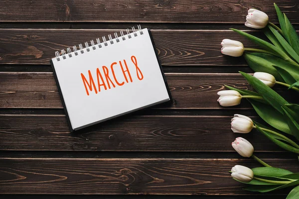 Flores blancas tulipanes sobre tablas de madera marrón. Tarjeta de felicitación con letras 8 de marzo — Foto de Stock