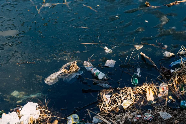 VICHUGA, RUSIA - 21 DE ABRIL DE 2019: Varias basuras y desechos de botellas y bolsas de plástico en el agua y en la orilla del río — Foto de Stock