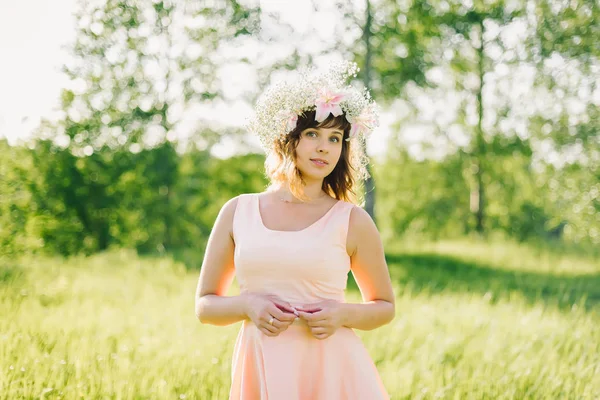 Hermosa chica con una corona de flores en su cabeza sonriendo al aire libre en un día soleado — Foto de Stock