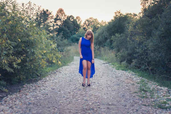 Chica en vestido azul posando sobre un fondo de puesta de sol — Foto de Stock