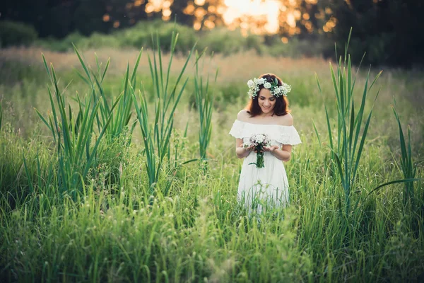 Meisje in een witte jurk met een krans en een boeket van bloemen — Stockfoto