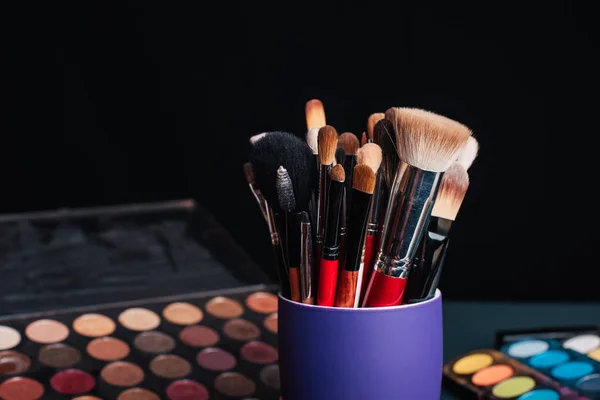 Conjunto de escovas de maquiagem profissional em um fundo de paleta com sombras coloridas — Fotografia de Stock