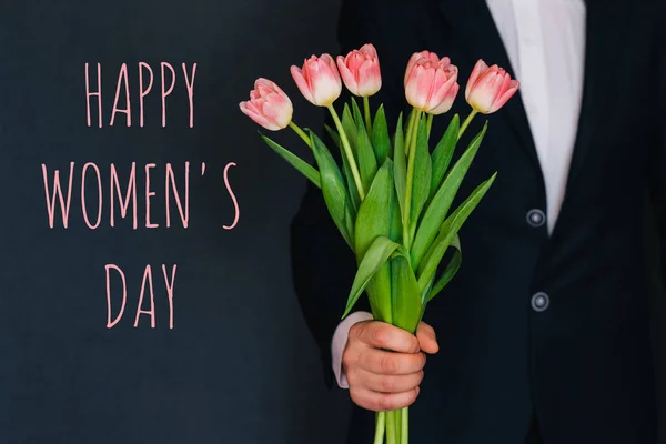 Ο άνθρωπος δίνει ένα μπουκέτο ροζ λουλούδια τουλίπες. Ευχετήρια κάρτα με κείμενο χαρούμενη ημέρα της γυναίκας — Φωτογραφία Αρχείου