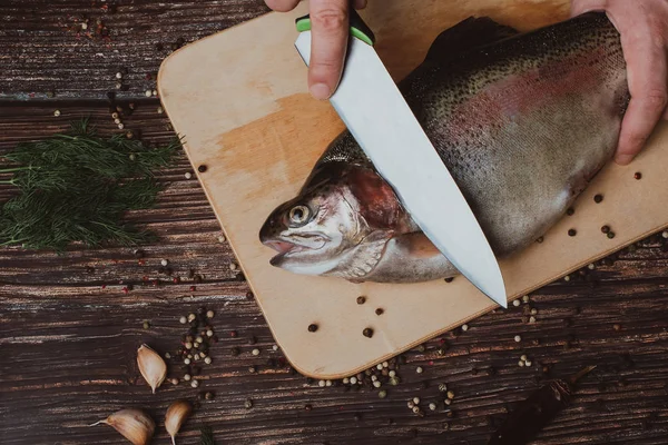 Manliga kocken skär råa öring på en träskiva i köket. Rå fisk för matlagning — Stockfoto