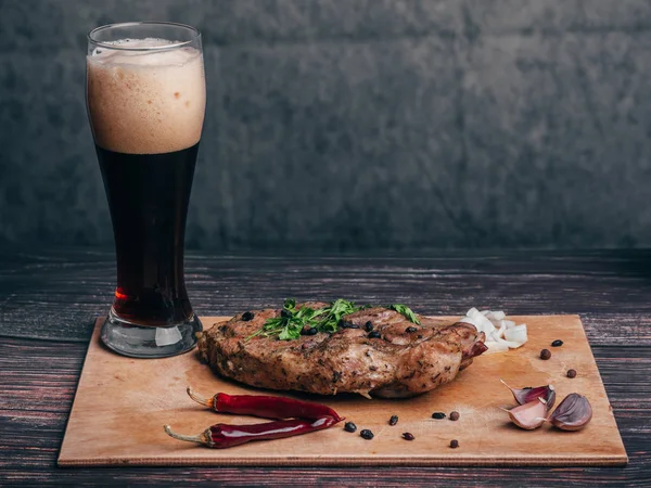 Gekookt varkensvlees met een glas donker bier en andere ingrediënten op een houten plank — Stockfoto