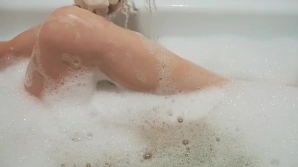 Красива брюнетка дівчина сексуально пестить ногу і співає у ванній кімнаті з піною — стокове відео
