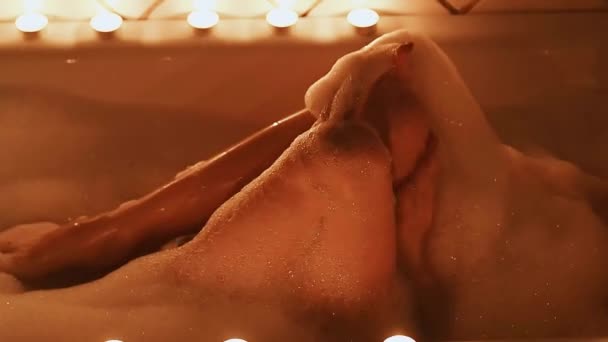 Menina morena nua acaricia sexualmente suas pernas e goza no banheiro com espuma com um copo de champanhe — Vídeo de Stock