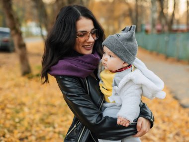 Genç, güzel, beyaz bir kız annesi gülümsüyor ve küçük oğlunu kucağına alıyor.