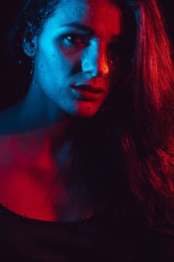 Kırmızı mavi aydınlatma ile yağmur damlaları ile cam arkasında güzel kızın şehvetli portre