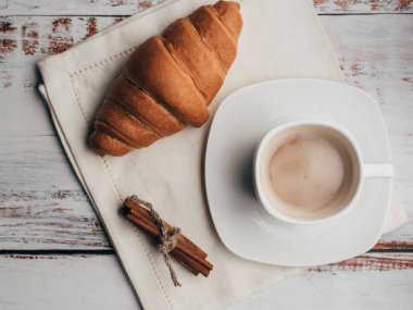 Fincan kahve ve kruvasan tarçın ile peçete ahşap bir masa üzerinde sopa