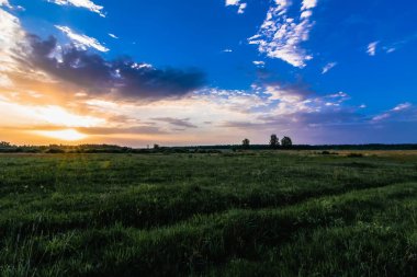 bulutlu bir gökyüzü ve çayır üzerinde gündoğumu veya günbatımı ve güneş ışınları ile bir alanda yaz manzara