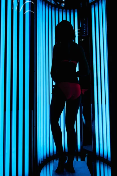 Girl in the vertical Solarium. Silhouette on the background of ultraviolet lamps — Stock Photo, Image