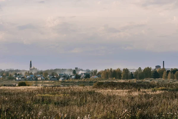 Jesienny krajobraz z polem i rzeką i Kościołem chrześcijańskim na horyzoncie — Zdjęcie stockowe